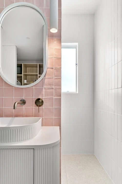 Inspiratiebeeld met roze badkamertegels, een ovale spiegel en een witte wastafel